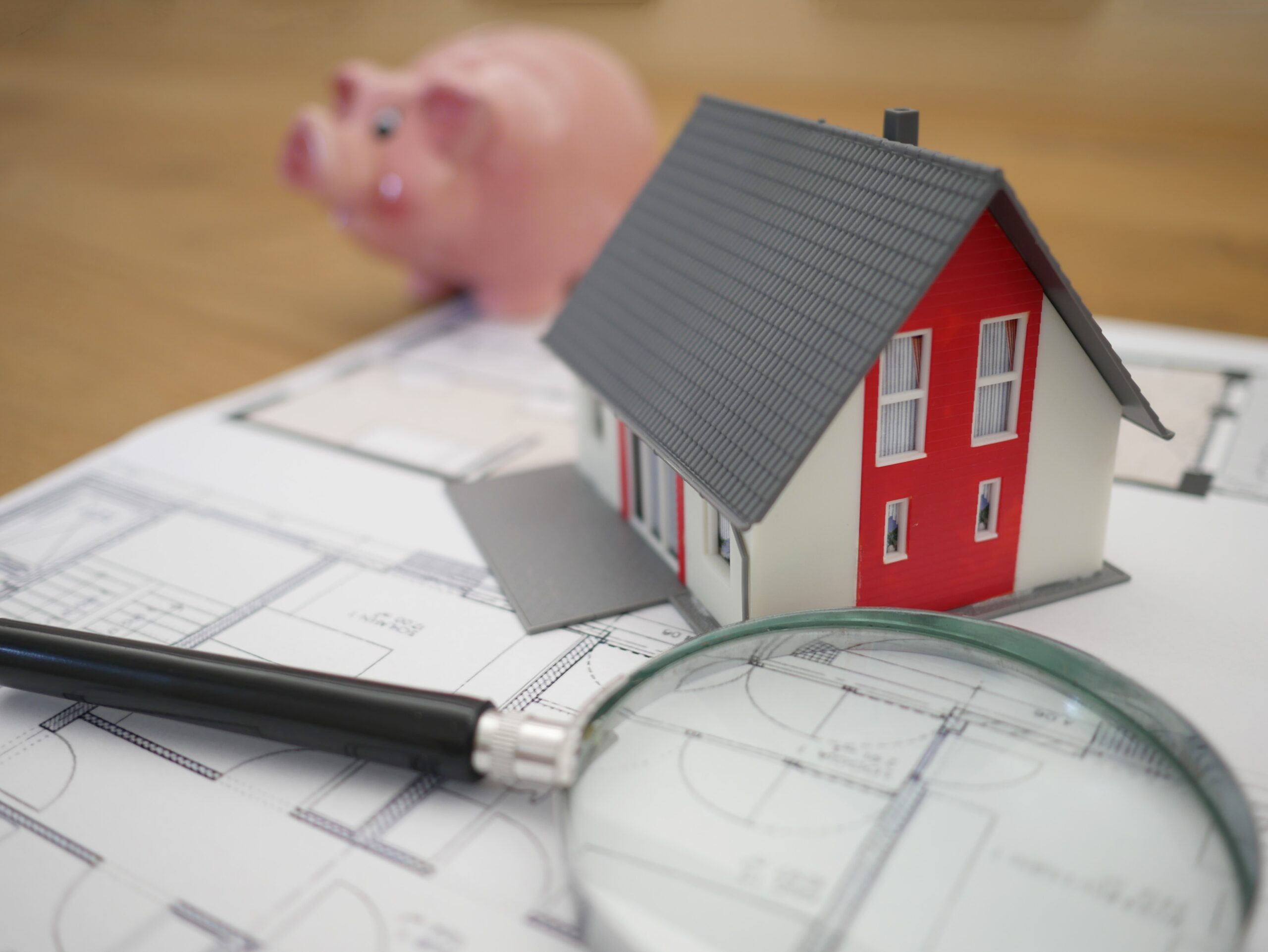 Stock image: Piggy bank, model house and magnifying glass laying on building plans